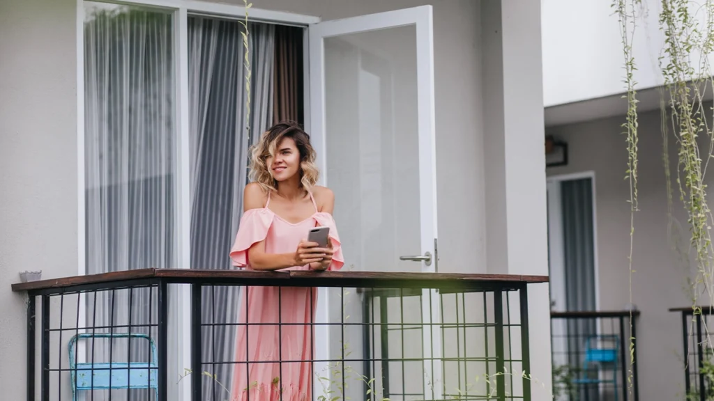 A woman standing on her balcony and open casement windows behind  her