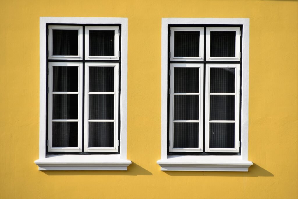 Twin flush white casement windows installed on vibrant yellow house exterior